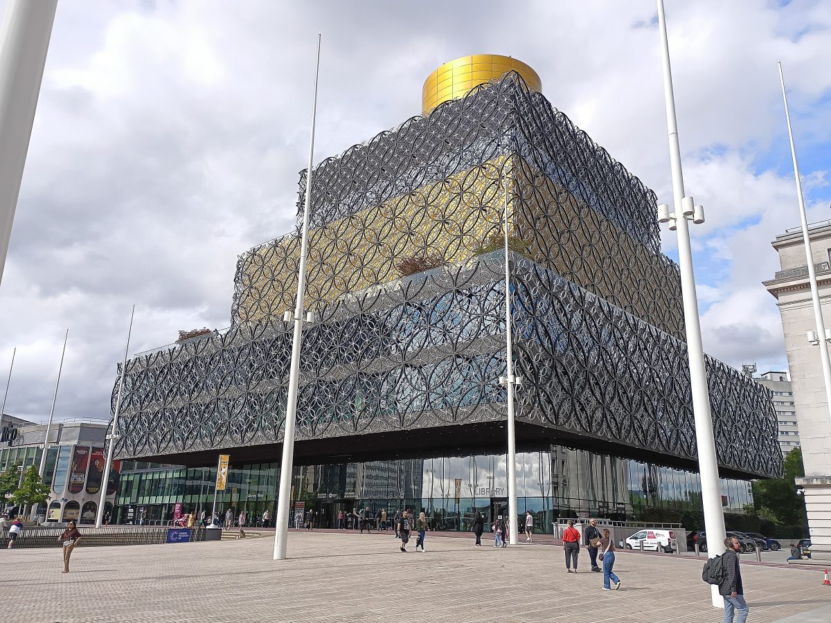 The Library of Birmingham, with its gold and silver metal lattice facade, seen across a paved square