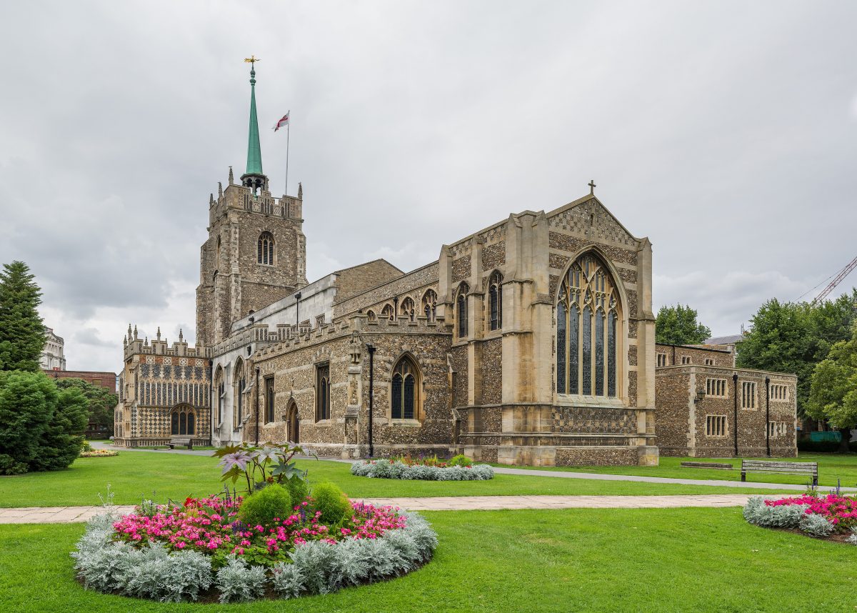 Chelmsford Cathedral with its flint walls, tower and green spire, behind flower beds in the churchyard