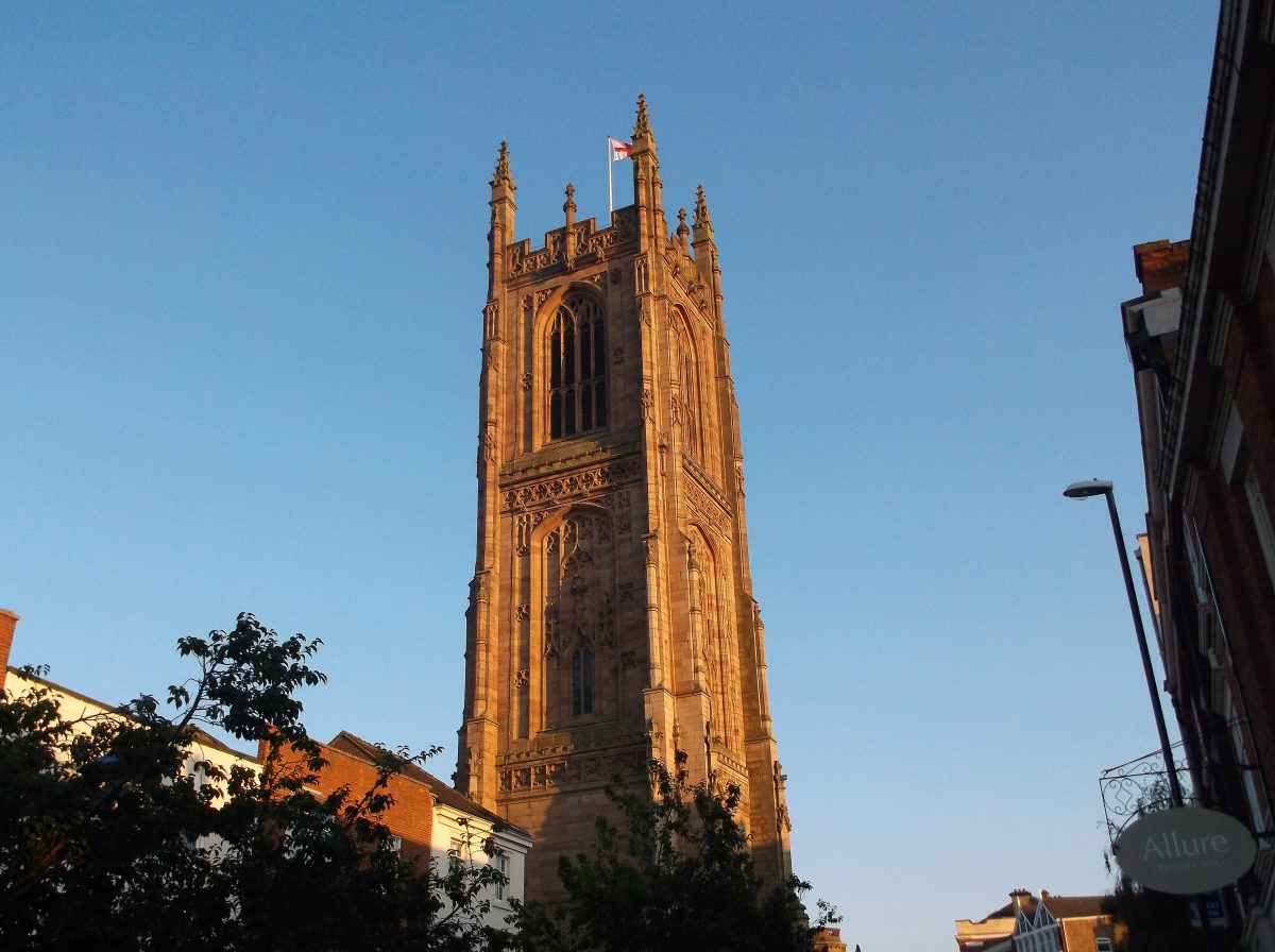 The Gothic tower of Derby Cathedral lit by evening sun against a clear blue sky