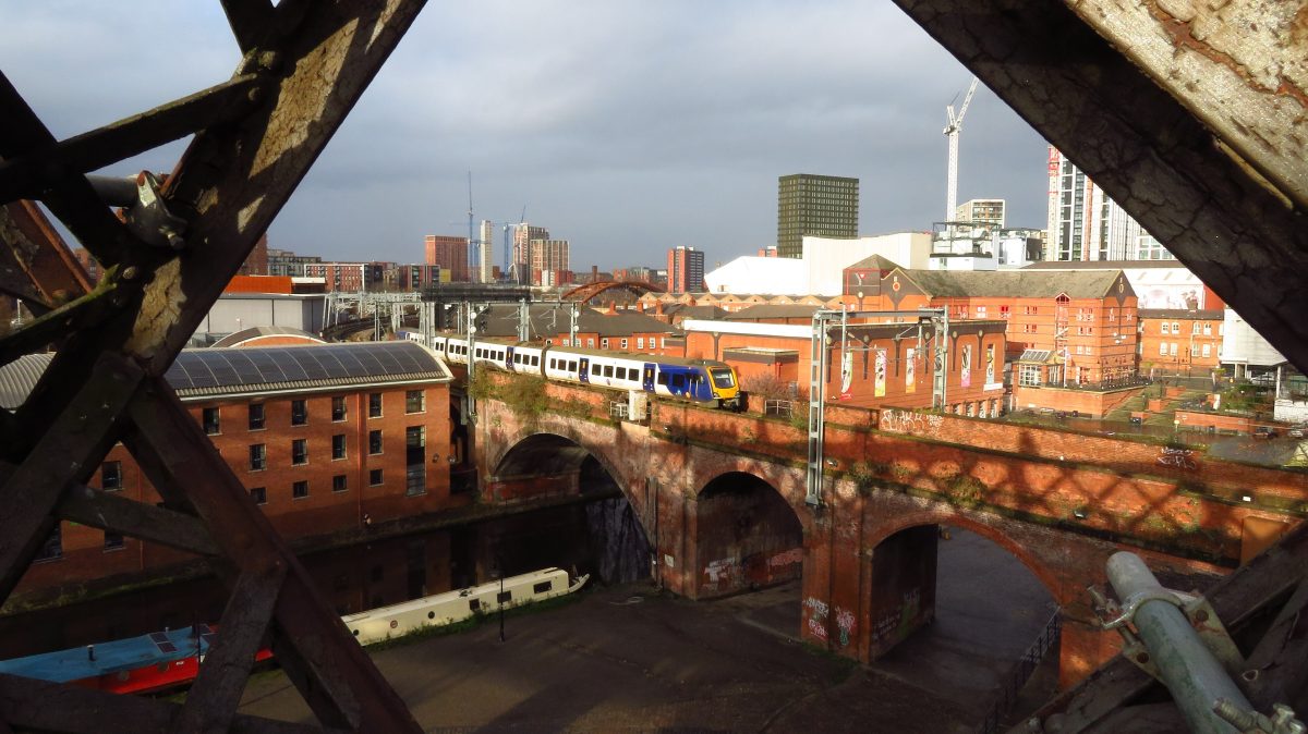 A train crossing a brick railway viaduct in Castlefield, Manchester, seen through the iron girders of Castlefield Viaduct