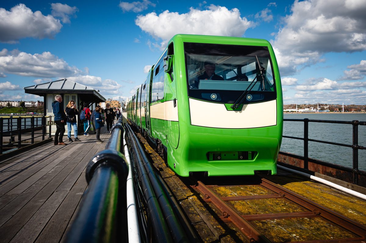 A green Southend Pier Railway train on the long wooden pier, with the Southend seafront in the distance