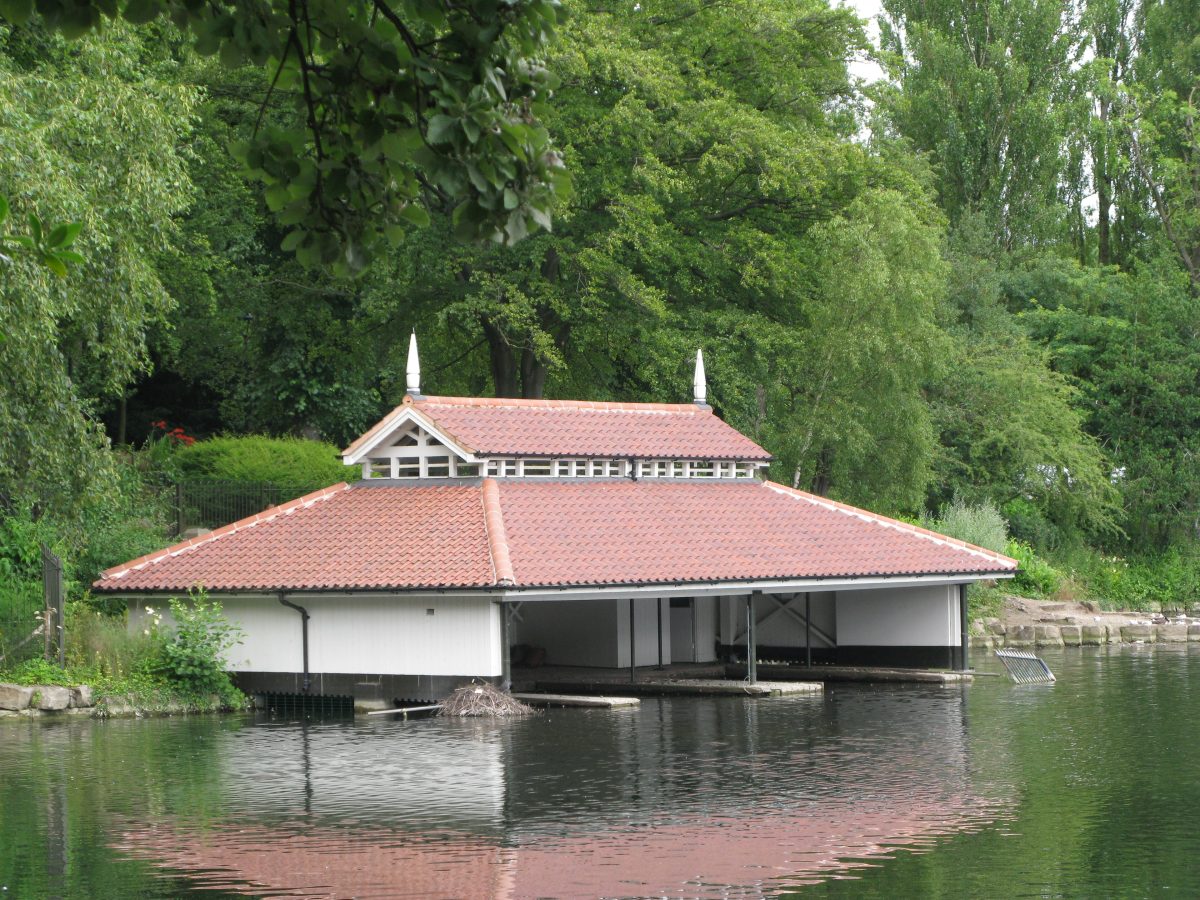 The white boat house with a red tiled roof on the lake at Walsall Arboretum, surrounded by trees